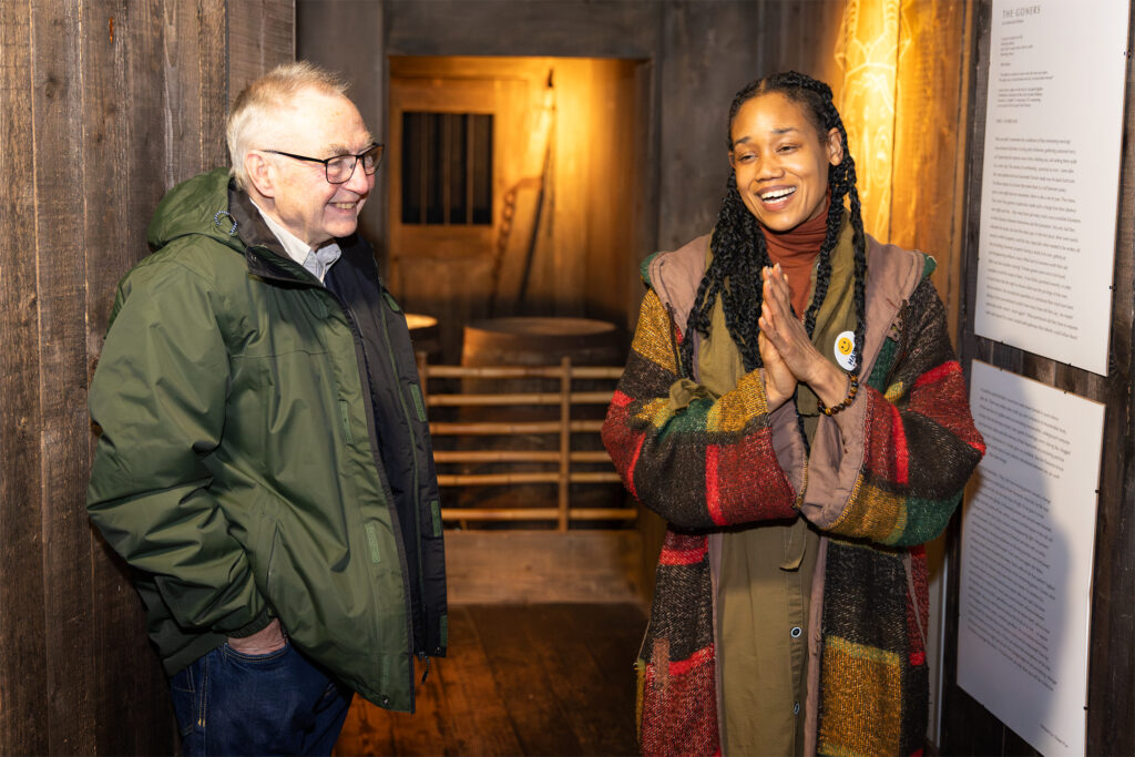 Photo of a man and woman talking and smiling next to some poetry o the wall in The Rum Story