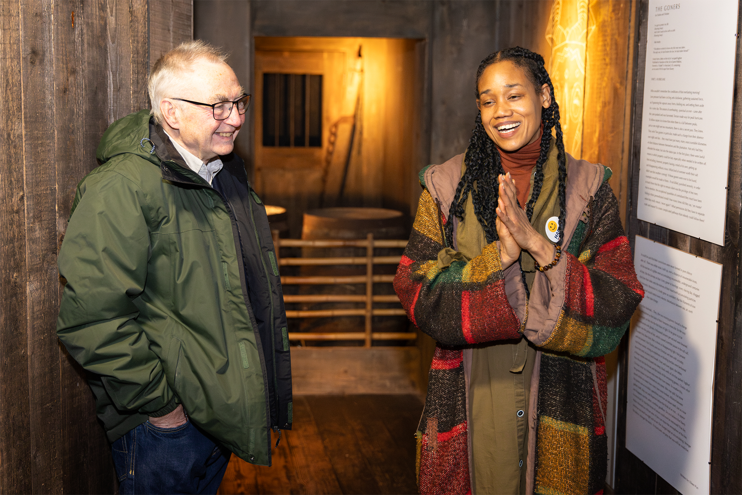 Photo of a man and woman talking and smiling next to some poetry o the wall in The Rum Story